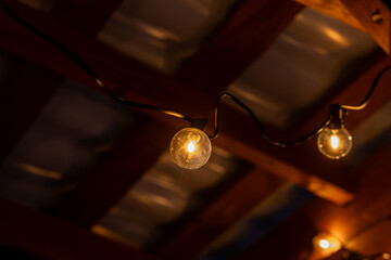 LED string lights hang under a wooden terrace roof with visible beams and a corrugated metal...