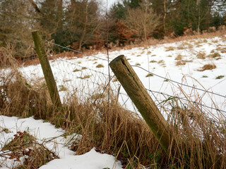 Snow-covered field with wooden fence and dried grass in a winter landscape.