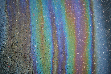 Colorful oil slick on pavement creates a captivating rainbow effect in urban setting.