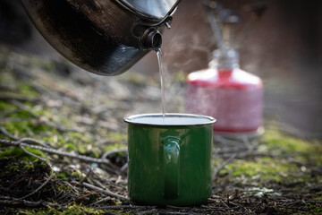 Heißes Wasser wird in Campingtasse gefüllt, Gaskocher im Hintergrund in der Unschärfe