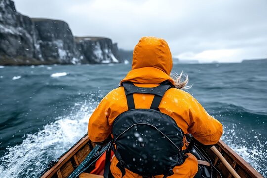 A person in an orange jacket is paddling a boat in the ocean - Powered by Adobe