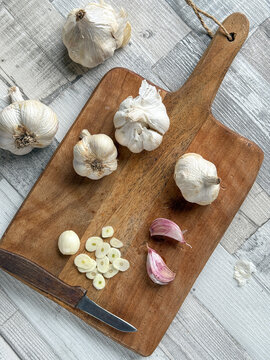 Fresh organic garlic bulbs and sliced clove on wooden cutting board. Overhead view