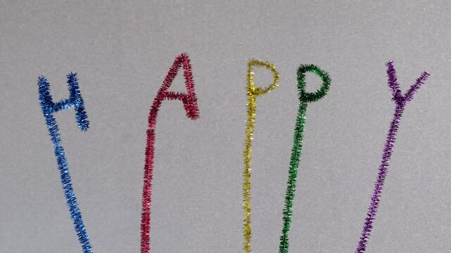 Swinging Happy text with sparkling colorful letters made by pipe cleaners or whistle washer, chenille wire, sparkling white background