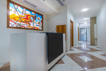 The reception desk features a modern, vibrant stained glass design, elegant decor and natural light in a spacious office hallway.