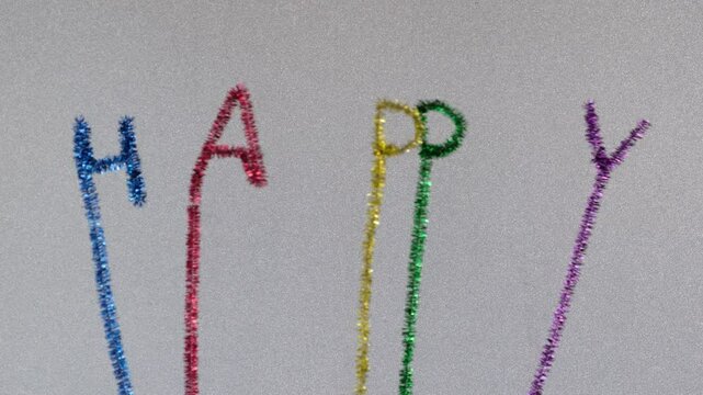 Swinging Happy text with sparkling colorful letters made by pipe cleaners or whistle washer, chenille wire, sparkling white background