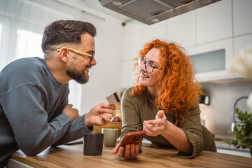 smiling couple use cellphone and credit card shopping online at kitchen