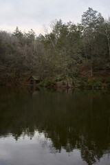 Small shed on the shore of a calm lake with trees reflected. 