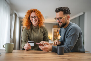 smiling couple use cellphone and credit card shopping online at kitchen
