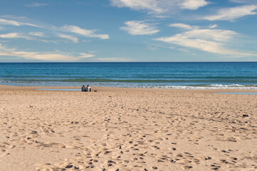 YOUNG couple sitting on the edge of Muchavista beach IN THE SAND, EL CAMPELLO, Alicante, Spain