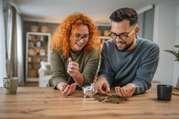 Adult happy couple save money coins in the piggy bank at home