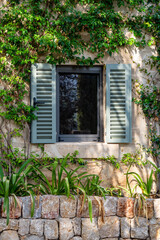 El Calvari in Pollensa, Mallorca, Balearic Islands, Spain. The window of the house located right next to the chapel. Shutters in the window and a stone wall with flowers.