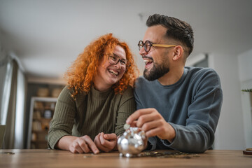 Adult happy couple save money coins in the piggy bank at home