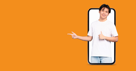 A young person with a friendly smile gestures towards the viewer while holding a large smartphone in front of an orange background, highlighting modern communication and technology trends.