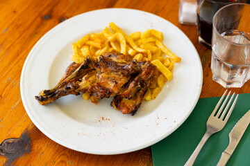 Delicious dinner of baked young rabbit leg served with side dish of crispy french fries on white plate..