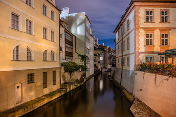 The Certovka Canal glistens under the night sky in Prague, with historic buildings lining its banks. Soft light illuminates the water, creating a serene atmosphere perfect for evening strolls.