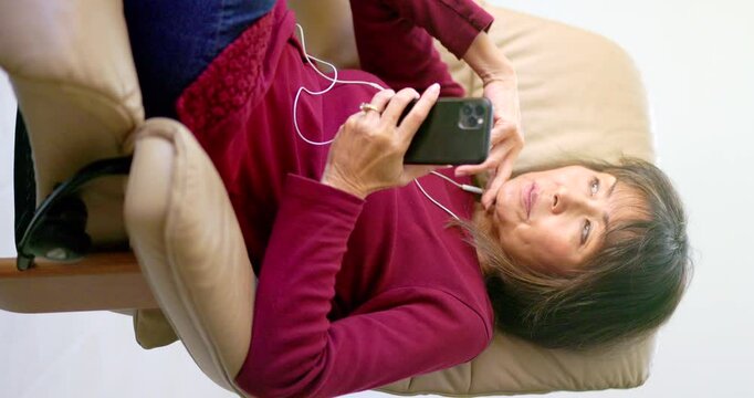 Woman wearing earphones relaxing enjoying listening to smartphone music vertical video