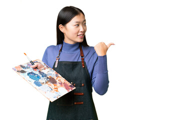 Young artist woman holding a palette over isolated chroma key background pointing to the side to...
