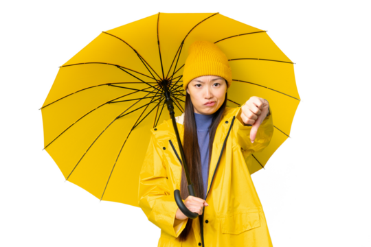 Young Asian woman with rainproof coat and umbrella over isolated chroma key background showing thumb down with negative expression