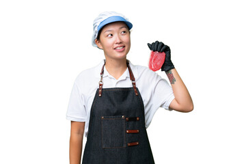 Young caucasian woman wearing an apron and serving fresh cut meat over isolated background thinking an idea while looking up