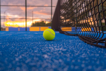 a lonely paddle tennis ball in a blue paddle tennis court at sundown, background for racket sports...