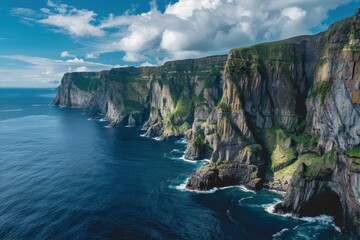 Dramatic coastal cliffs rise above serene ocean waters under a bright sky with scattered clouds