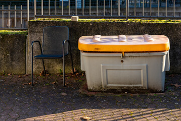Fototapeta premium Unused chair beside a storage container on a sunny day in an urban environment