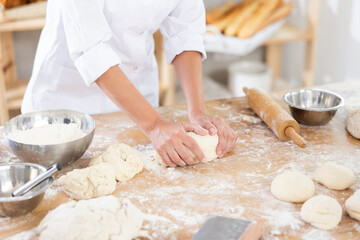 Female baker in uniform kneading raw dough close-up