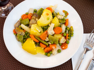 Lunch is served on dark brown tablecloth - vegetable salad menestra. Dish is made from carrots, potatoes, green peas, mushrooms and seasoned with spicy sauce