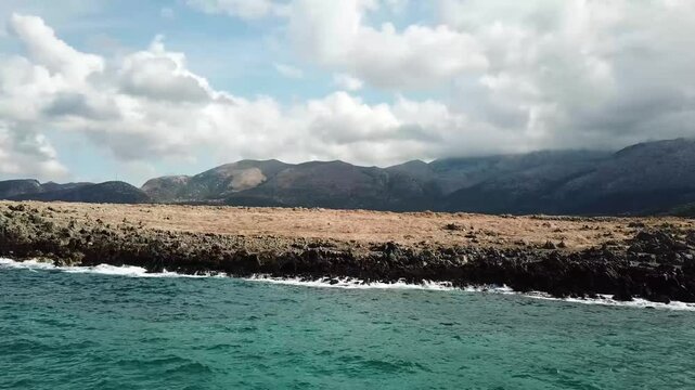 Drone Flight from the Sea Towards the Rocky Coastline Near Potamos Beach, Chersonisos, Crete &ndash; Aerial Views with Mountains in the Background Under the Midday Sun