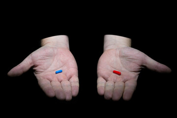 Сhoose your destiny concept. Male hands holding red and blue pills capsules on black background.