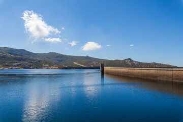 Obraz premium A large dam holds back a blue lake surrounded by mountains under a blue sky with scattered clouds