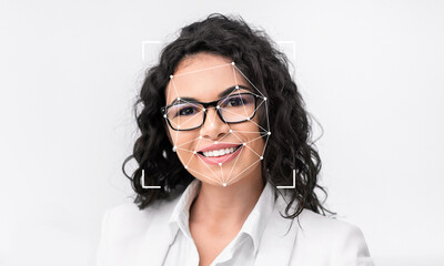 Obraz premium A smiling woman with curly hair and glasses stands confidently against a plain backdrop. Facial recognition technology is evident as geometric markers highlight her features.