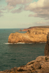 A scenic view of rugged coastal cliffs rising above the blue ocean under a cloudy sky