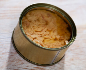 Open tin can of preserved fillet of bonito in oil on wooden table..
