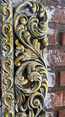 Ornate decorative molding with golden and ivory accents featuring intricate scrollwork details, placed against a textured brick background with a rustic, vintage aesthetic.