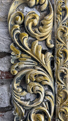 Ornate decorative molding with golden and ivory accents featuring intricate scrollwork details, placed against a textured brick background with a rustic, vintage aesthetic.