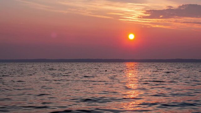 Aerial view footage B roll nature landscape background. round red sun rise up from horizontal at a peaceful sea in summer season. orange color sunset, sunrise sky reflect on water rapping gently.