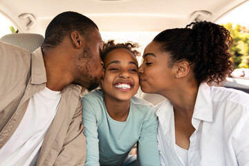 Obraz premium Cheerful Black Parents Kissing Daughter Sitting In New Car Riding Enjoying Road Trip Together. African American Family Having Summer Vacation And Traveling By Auto. Transportation Concept