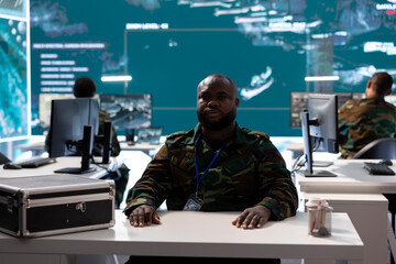 Military officer participates in a secure videoconference call in modern command center, transmitting live satellite information. Federal collaboration for national security operations.