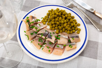 Pieces of herring served on plate with pea and scallion. Appetizer fish on table.