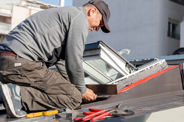 A roofer and window master work. The craftsman covers the skylight with sheet metal. Roofing tools.