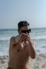 male person with beard and sunglasses doing exercises on the beach with bare torso 