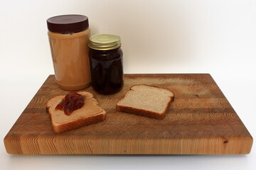 Peanut butter and jelly sandwich, being made on a cutting board before a white background