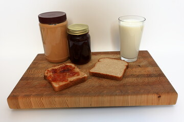 Peanut butter and jelly sandwich, being made on a cutting board before a white background