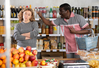 European wife and African husband, yells at each other. Angry man and furious woman screaming in shop. Couple find out their relationship near counter in store