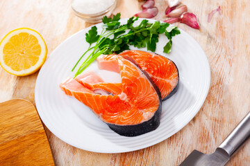 Raw salmon steaks on plate with garlic, lemon and parsley.