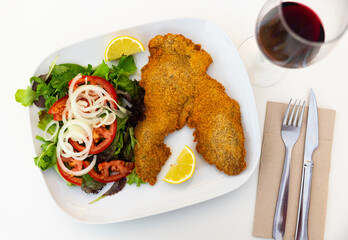Breaded pork with fresh salad with onions and tomatoes. Serving Spanish pork with vegetables on a white plate