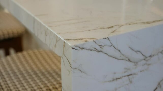 Close up of sleek, modern countertop made of polished marble with beautiful white base and intricate brown and gray veining. Elegant shiny surface looks pristine and luxurious