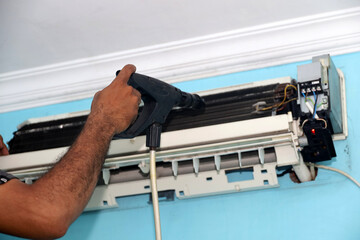 technician's hand cleaning home ac evaporator on wall, air conditioner maintenance concept.