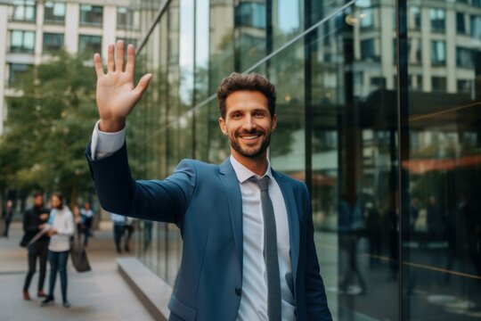 Portrait of a cheerful businessman waving his hand in greeting in front of modern office buildings